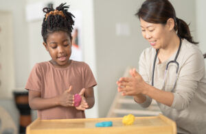 happy child playing with playdoh with her therapist