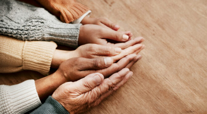 People, hands together and generations in care above on mockup for unity, compassion or trust on wooden table. Group holding hand in collaboration, love or support for community, teamwork or youth