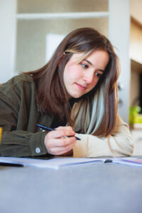 Teenage girl sitting at the table writing in notebook